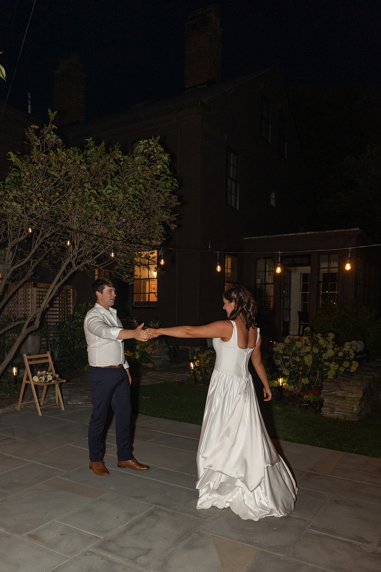 Couple sharing their first dance outdoors under string lights at night.