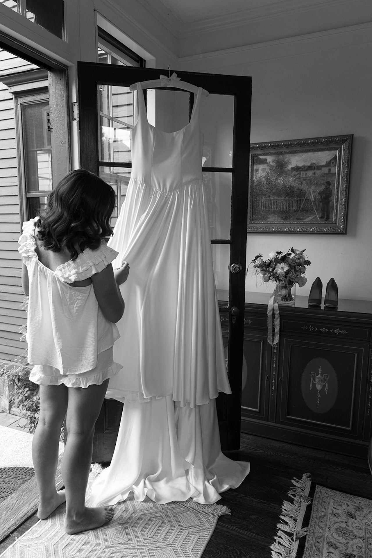 Bride admiring her silk gown hanging on a glass-paned door, a quiet getting-ready moment inside one of Maine’s Historic Wedding Venues.