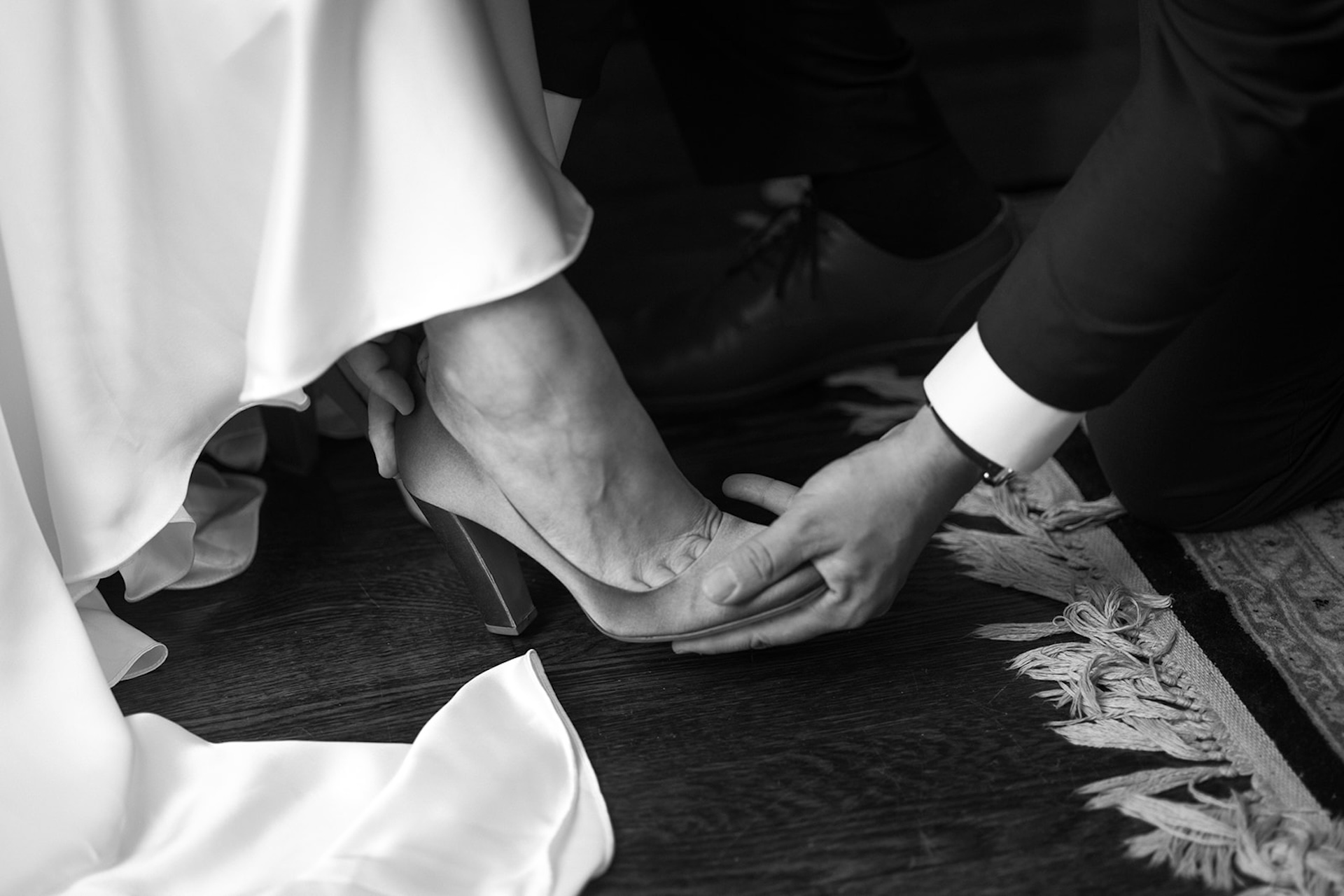 Close-up of the groom gently helping the bride slip into her heels, captured in a tender black-and-white moment inside a Historic Wedding Venue.