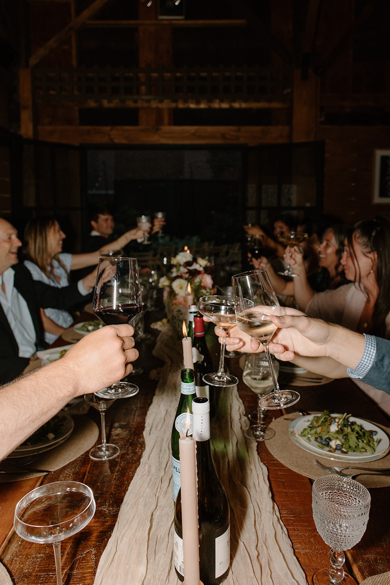 Guests raising their glasses around a long wooden table during an intimate evening celebration.
