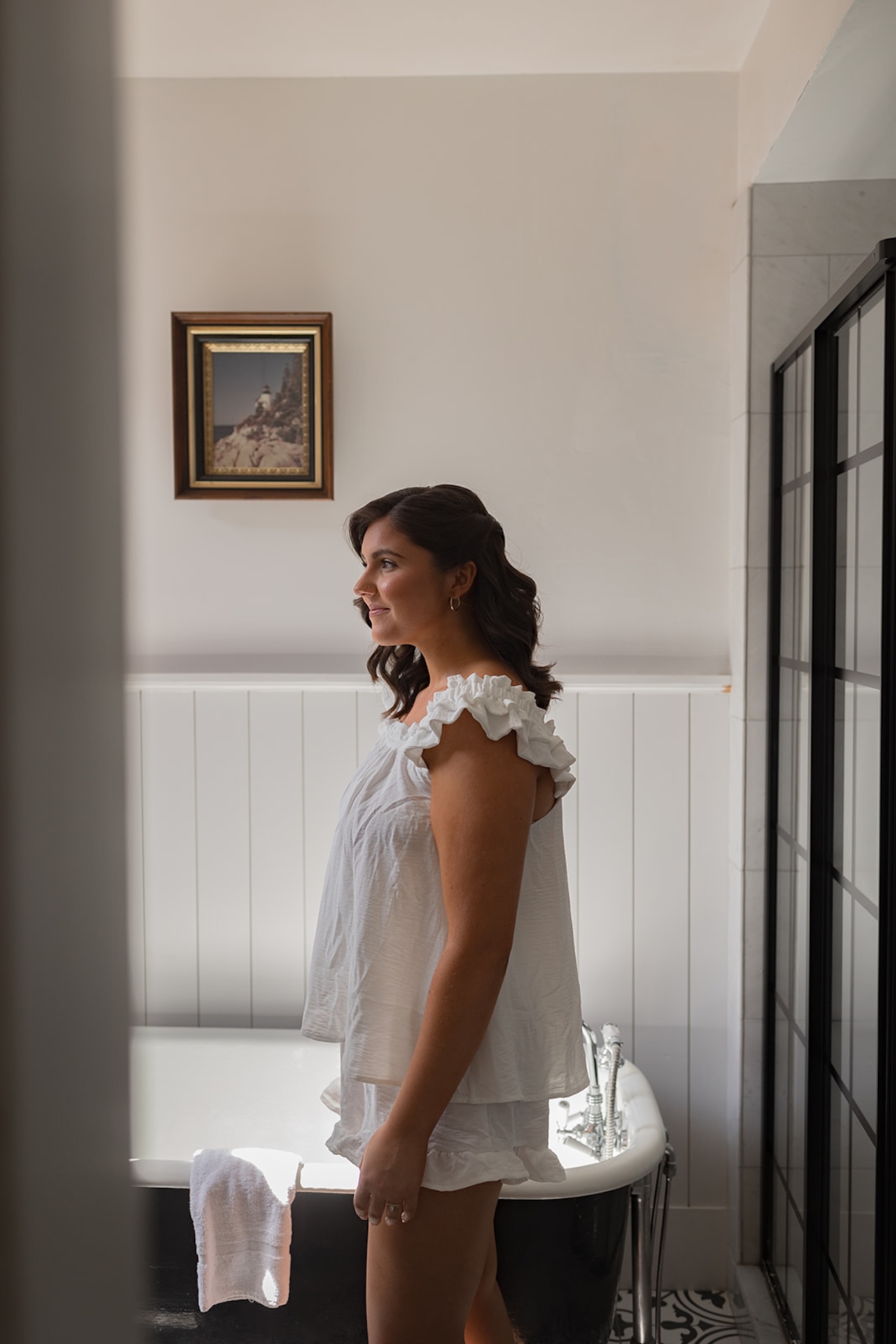 Bride standing in soft window light in her white ruffled pajamas inside a Historic Wedding Venue.