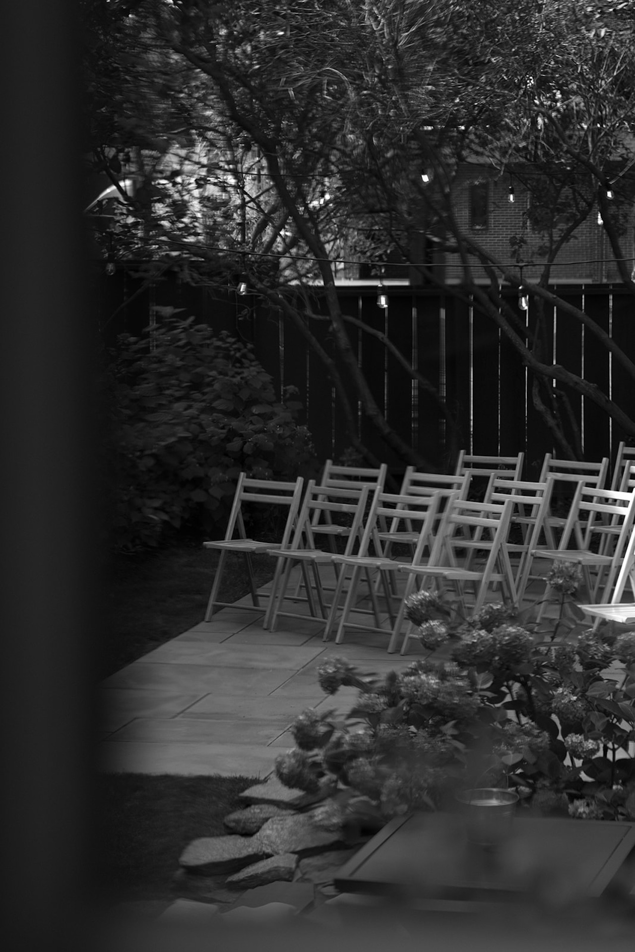 A quiet view of the ceremony chairs arranged in the garden, seen through branches and dappled afternoon light.