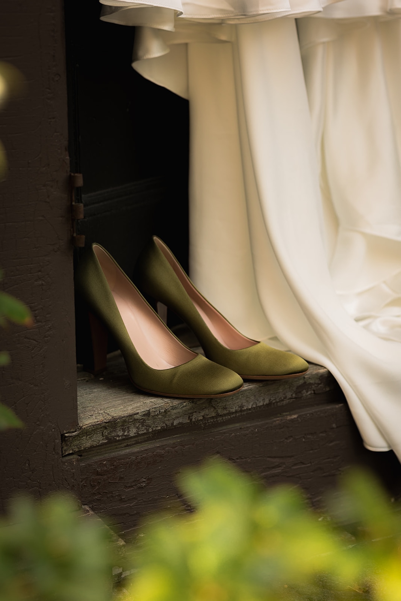 Close-up of the bride’s olive green heels resting against the wooden doorstep beneath her gown.