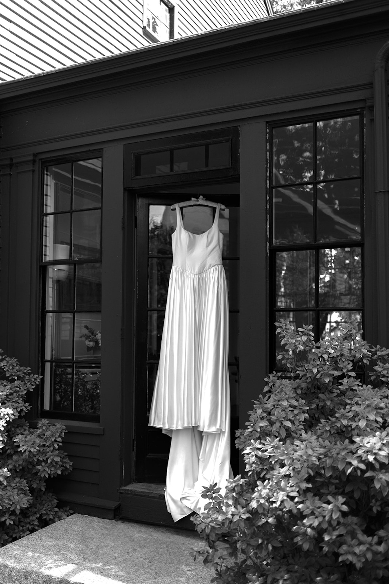Wedding dress hanging in the doorway of a historic home, framed by tall windows and garden greenery at one of Maine’s Historic Wedding Venues.