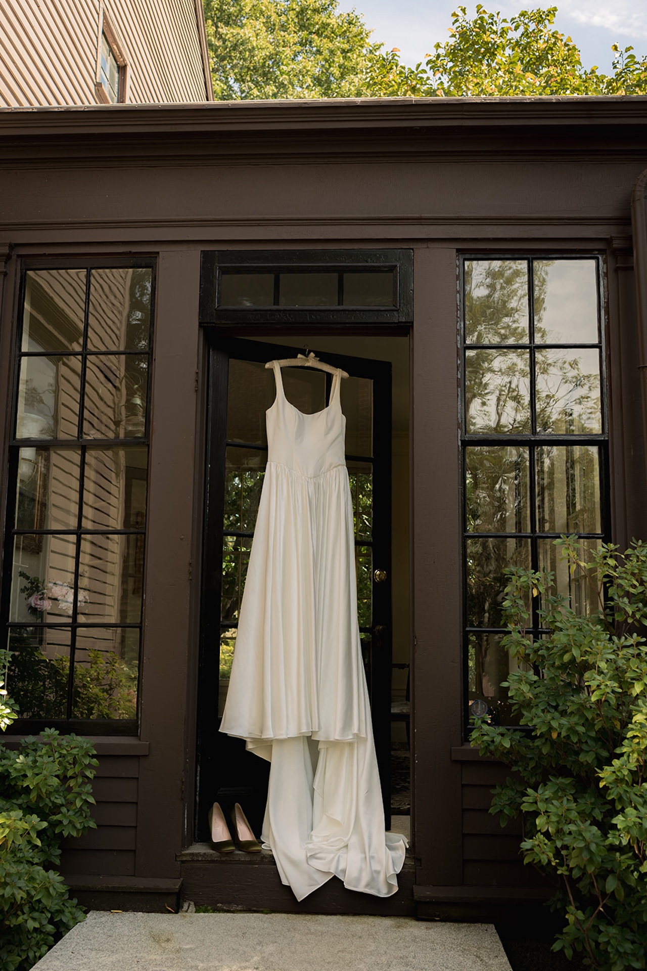 Wedding dress hanging in the doorway of a historic home, surrounded by tall windows and greenery.