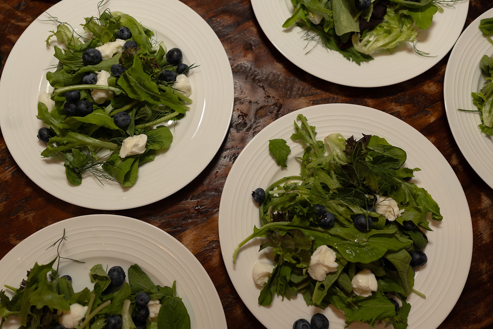 Plates of fresh summer salads with greens, blueberries, and mozzarella arranged on a wooden table at one of Maine’s Historic Wedding Venues.