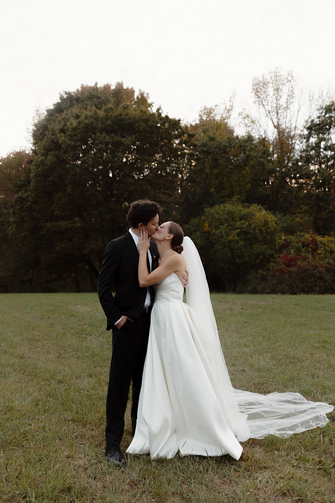 The couple shares a kiss in an open field at sunset, holding each other close.