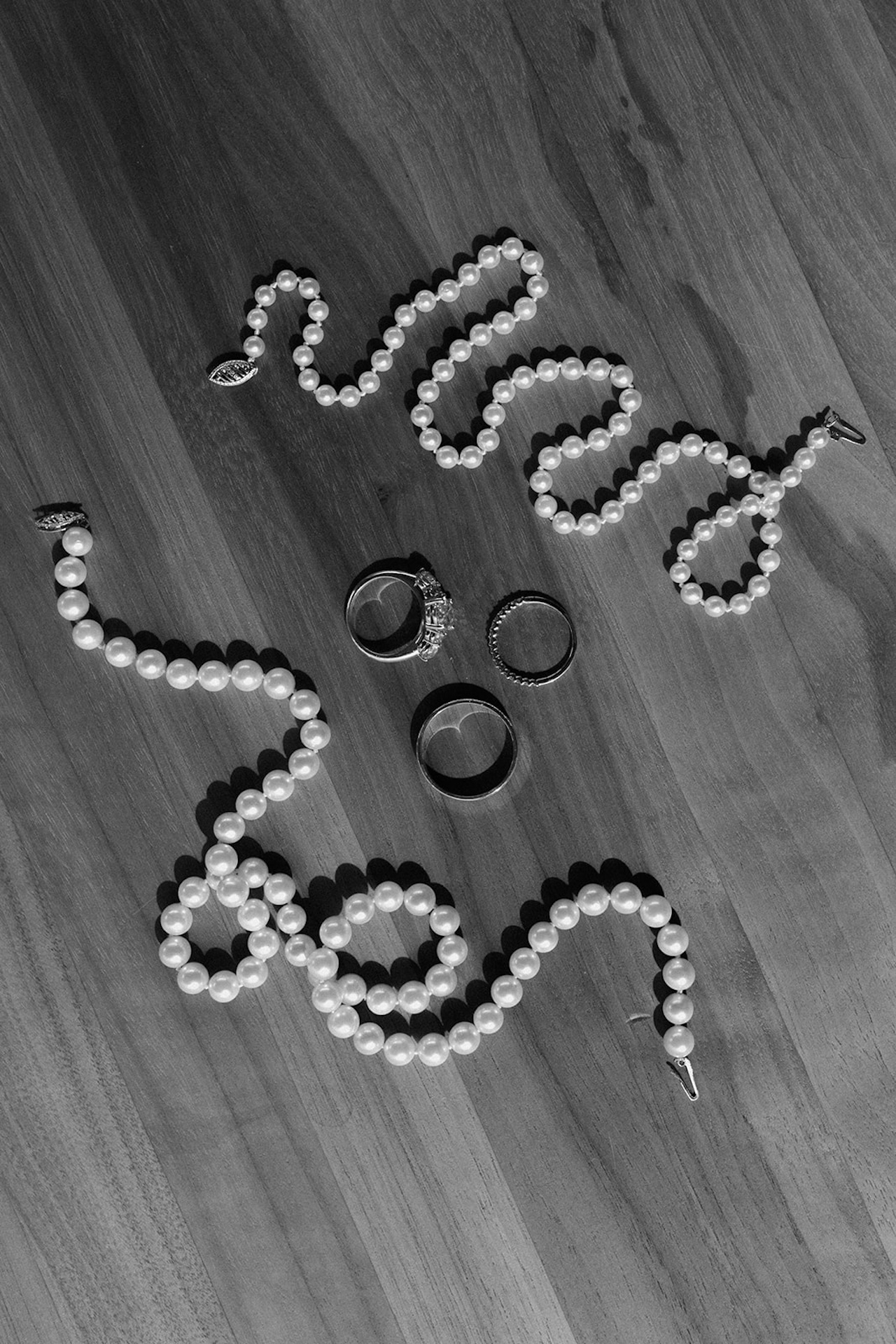 Black-and-white detail shot of pearl necklaces and rings laid on a wooden surface for a Wedding in Maine.