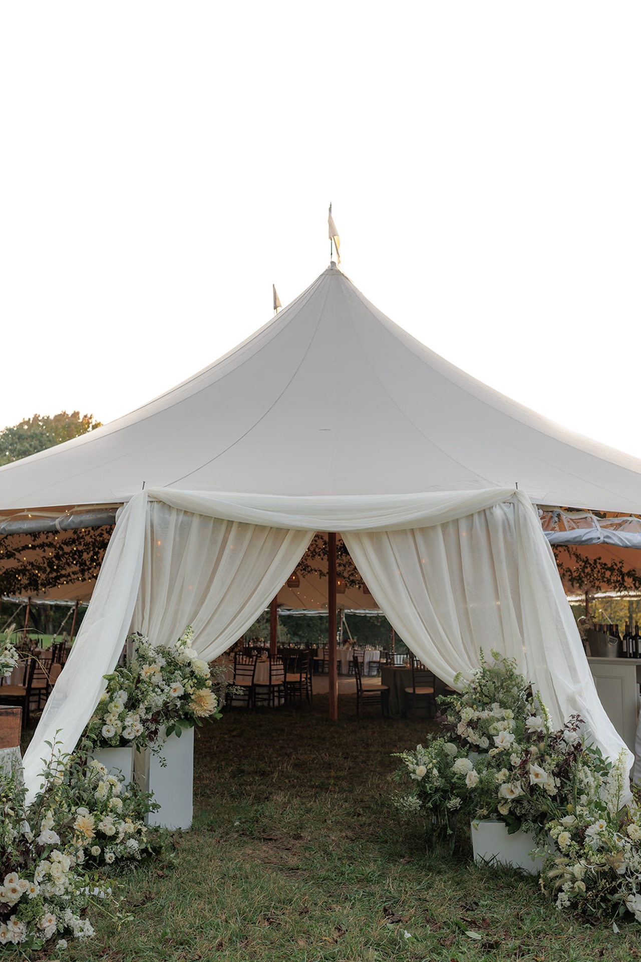 Grand sailcloth reception tent entrance draped with white fabric and overflowing florals.