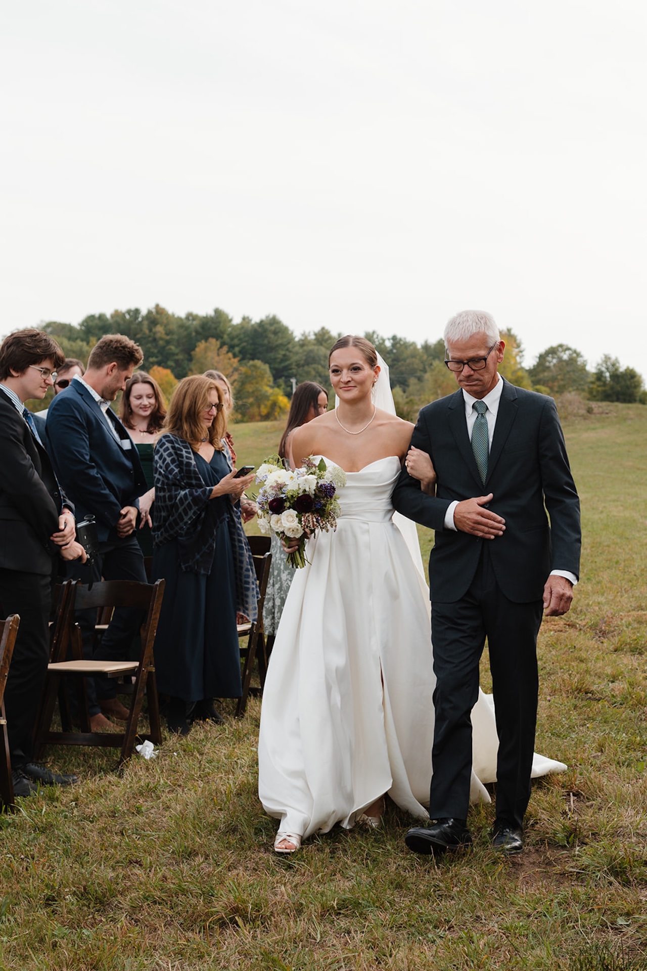 Bride walks down the aisle arm-in-arm with her father, holding her bouquet.