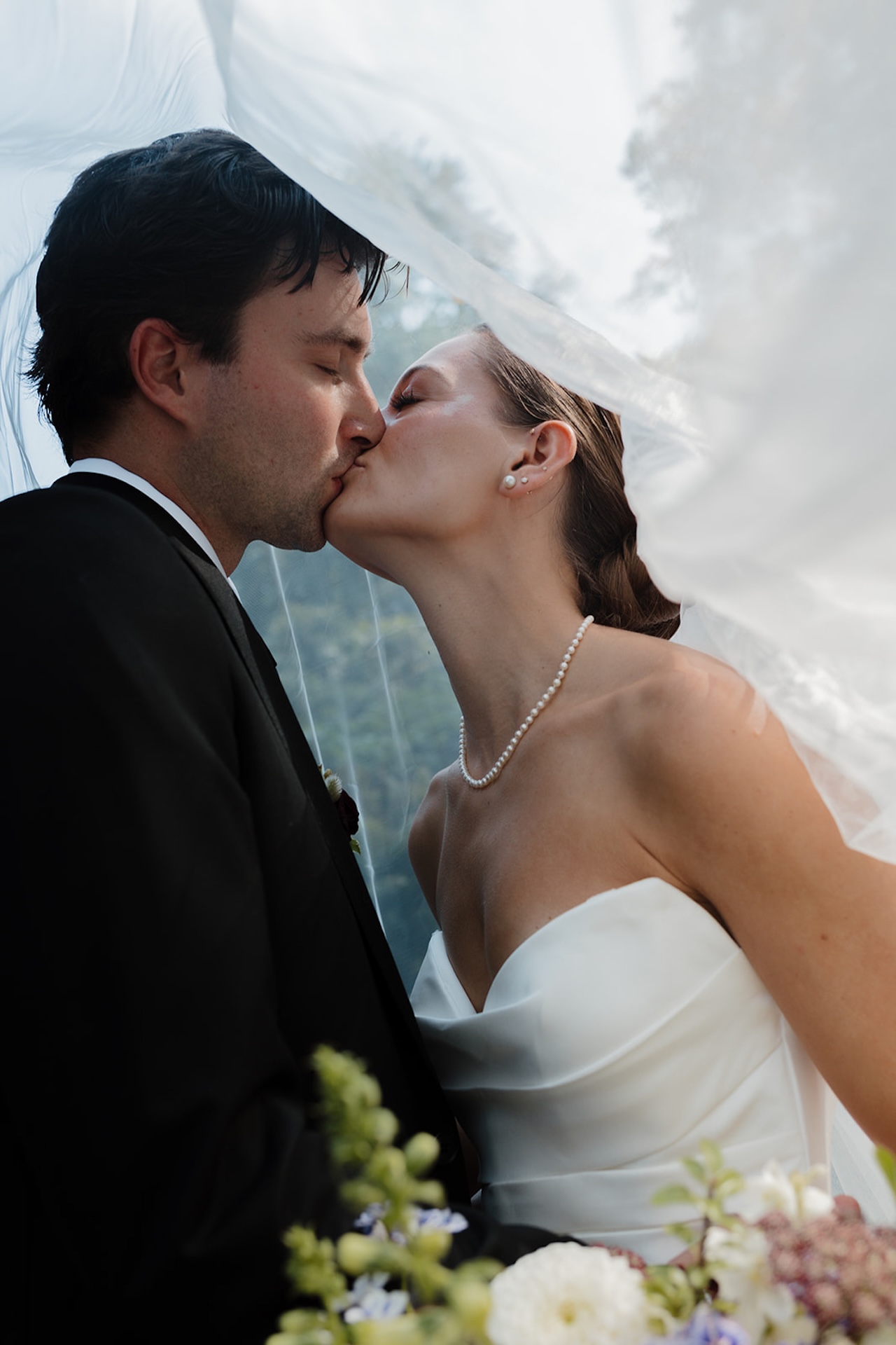 Couple stands in front of a modern home, lit by soft natural light at their Wedding in Maine.