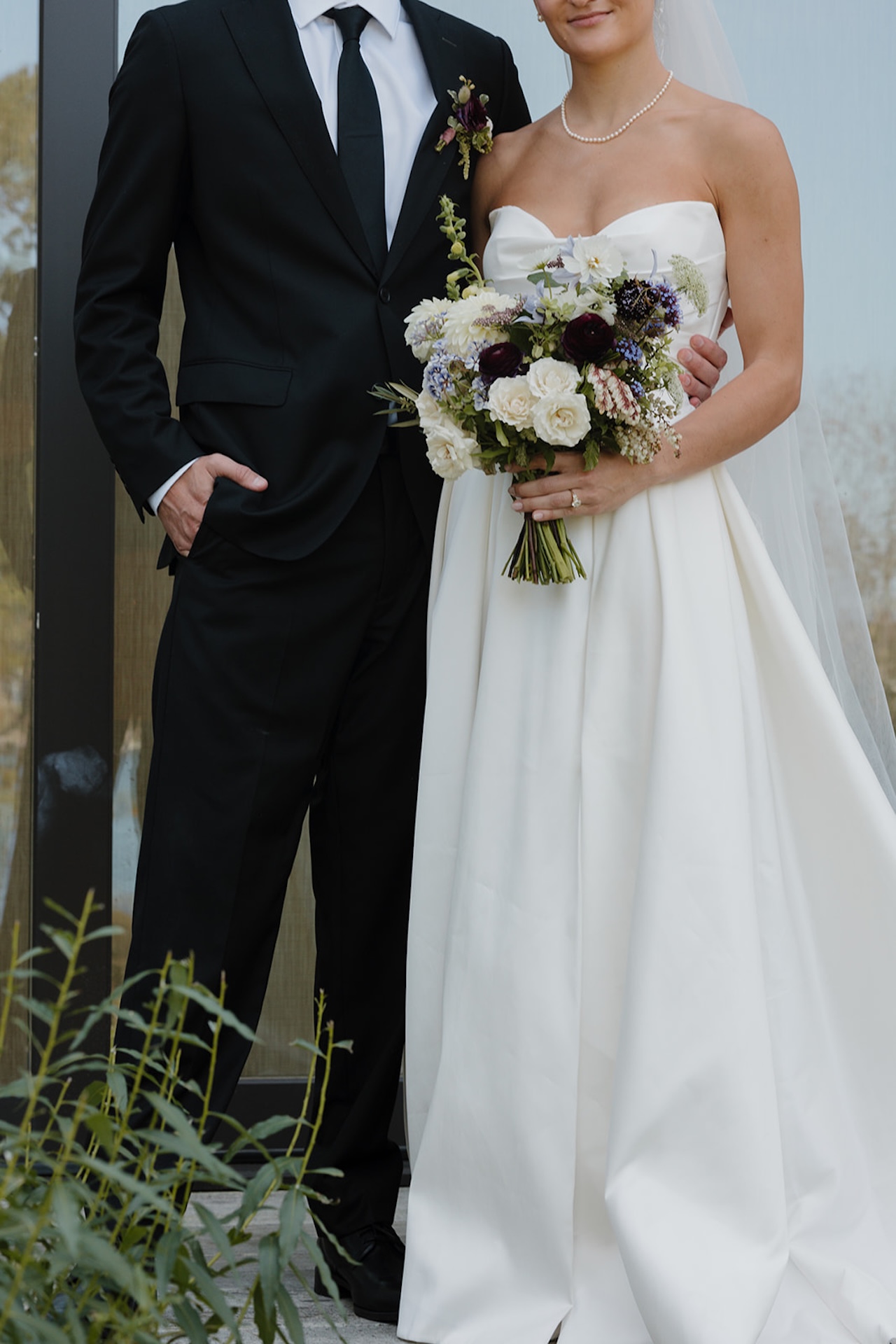 Cropped portrait of the couple holding the bridal bouquet, showing their attire and rings.