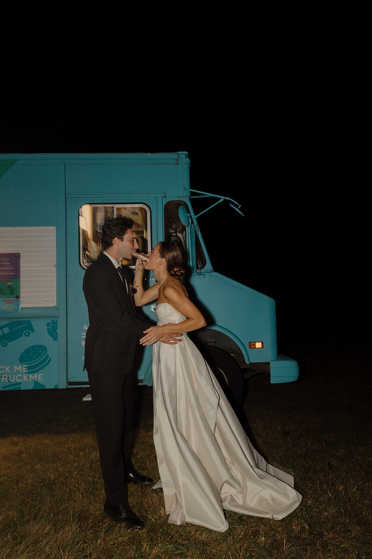 Bride feeds the groom a treat in front of a teal food truck during their private estate wedding.