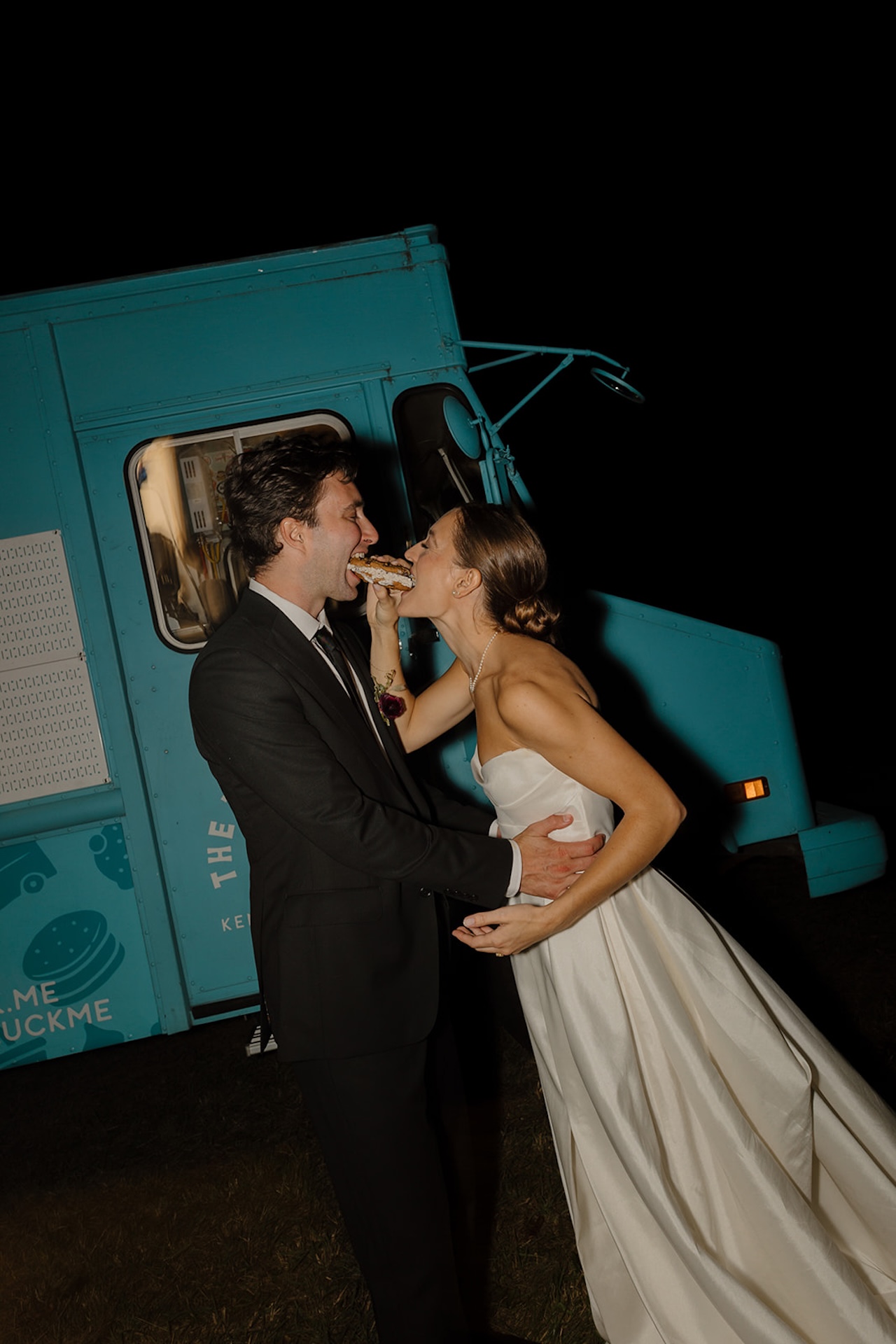 Bride and groom share a bite of a dessert in front of a teal food truck during their Wedding in Maine celebration.