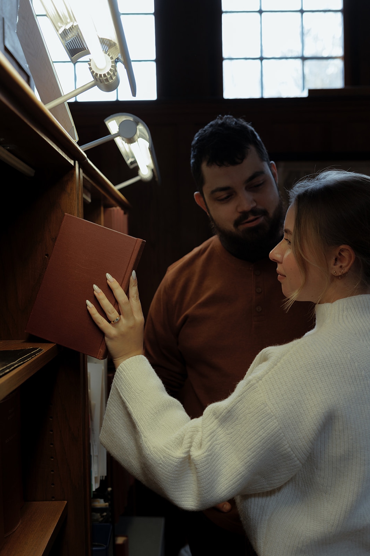 Close-up engagement portrait of a couple browsing books together in a library, creating intimate Engagement Photo Session Ideas with warm, cinematic light.