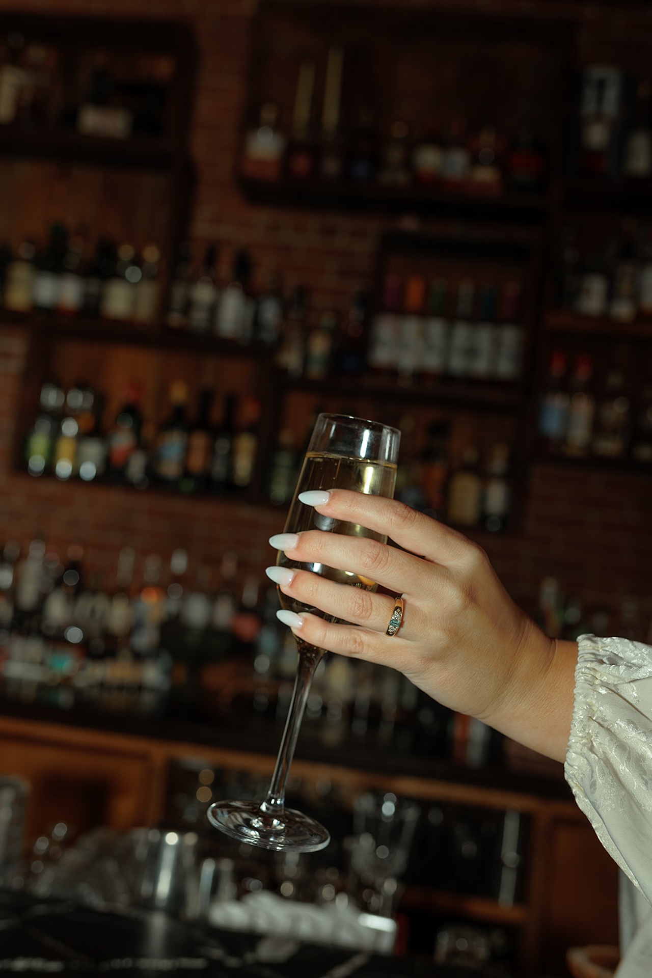 Detail engagement photo of a hand holding a champagne glass at a bar, showing an engagement ring as part of elegant Engagement Photo Session Ideas.