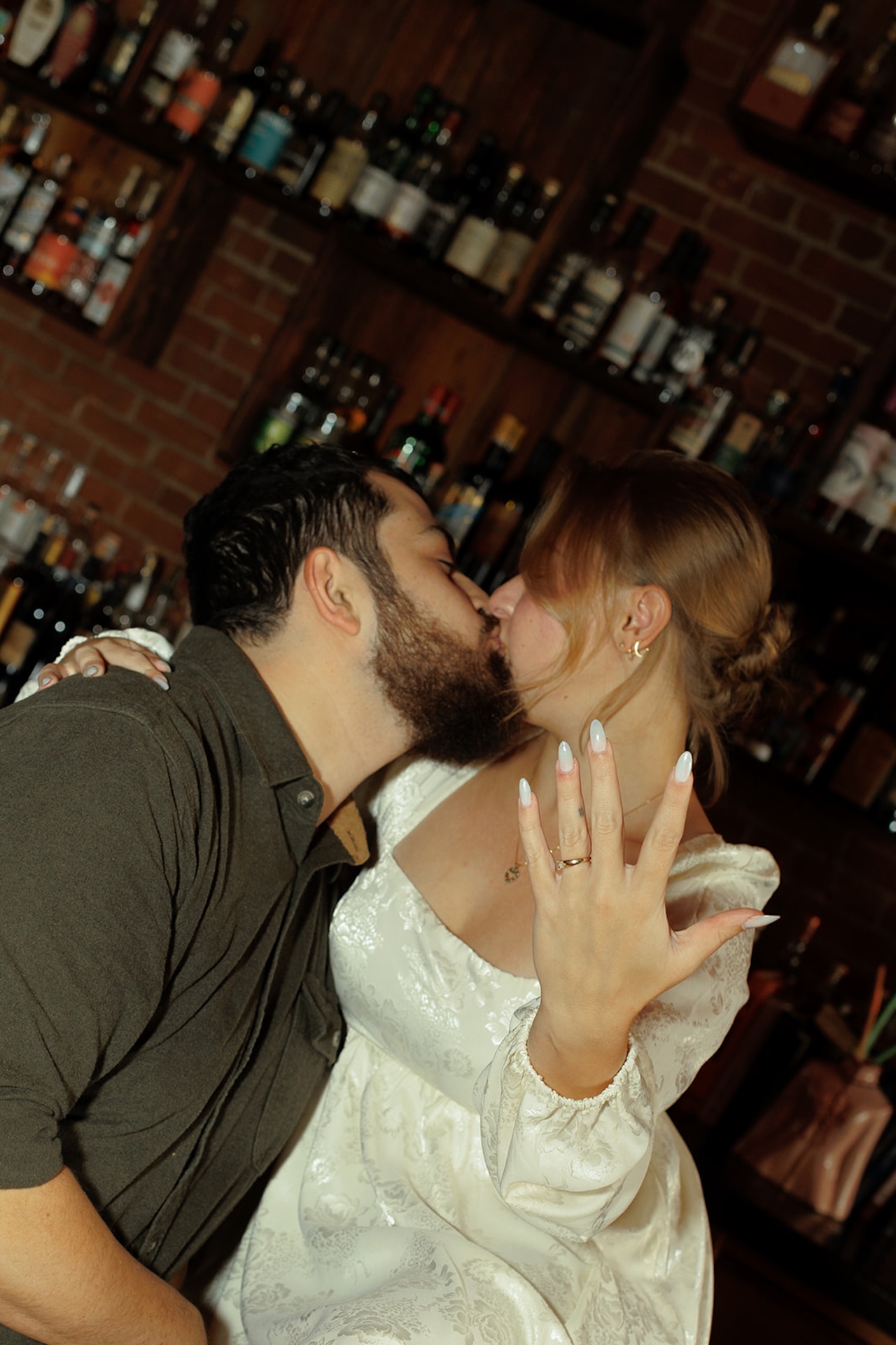 Romantic close-up of a couple kissing at a bar while showing off an engagement ring, a timeless example of Engagement Photo Session Ideas with personality.