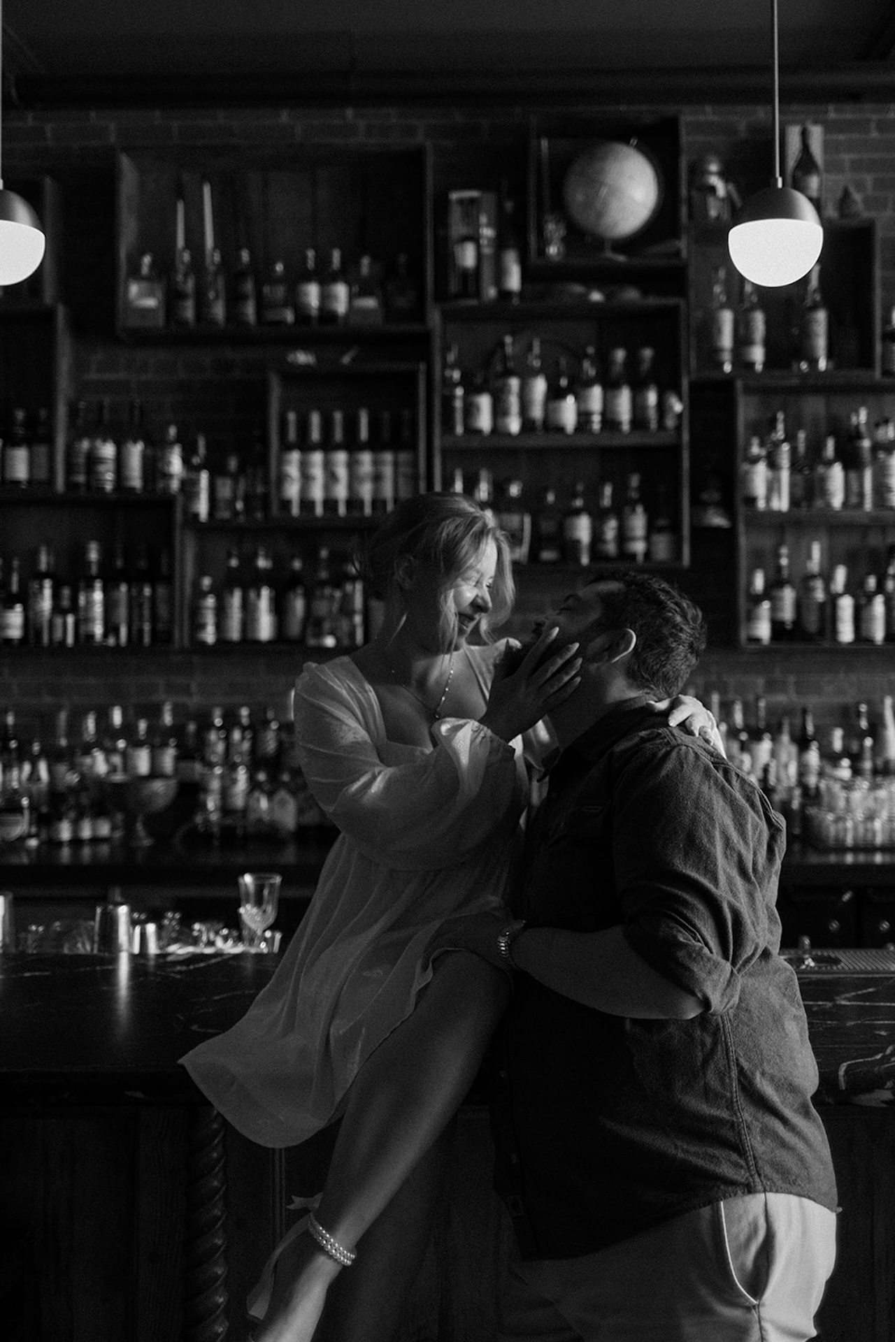 A black and white photo of a couple hugging and sitting together at a bar.