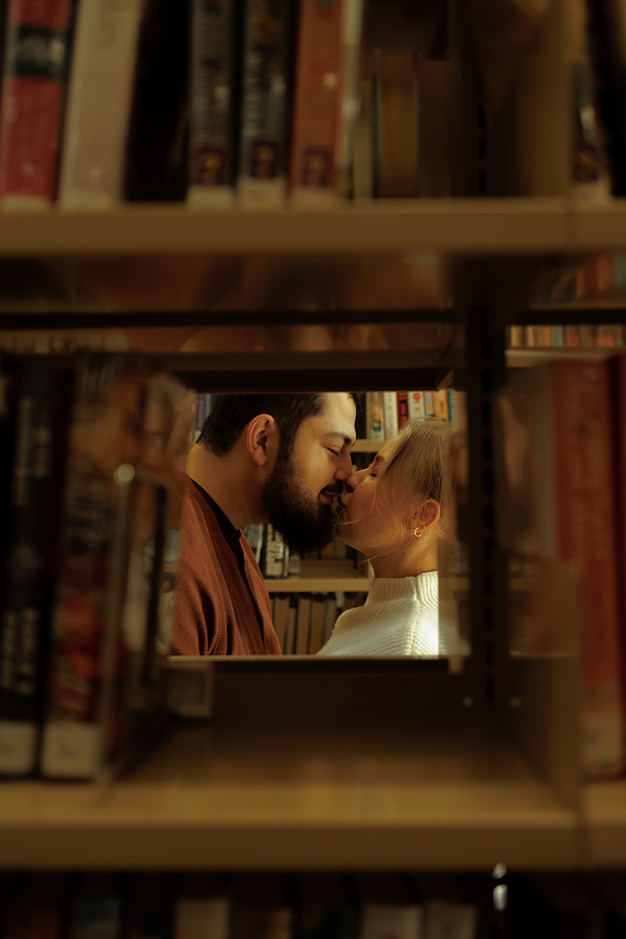 Intimate engagement photo of a couple touching foreheads between library bookshelves, capturing cozy Engagement Photo Session Ideas with a romantic editorial feel.