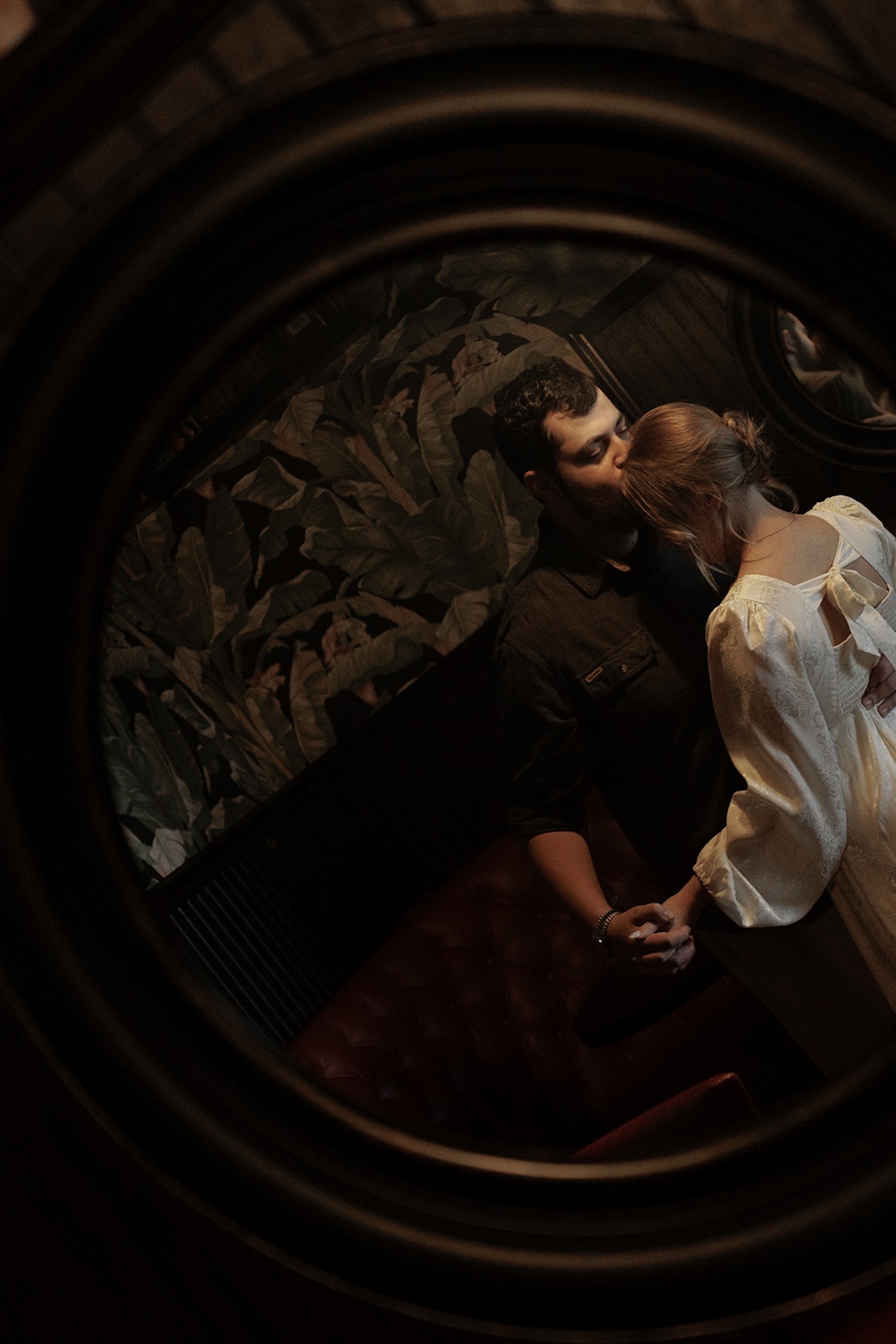 A unique couple photo of a ouple hugging and kissing in the hallway but shot through a mirror.