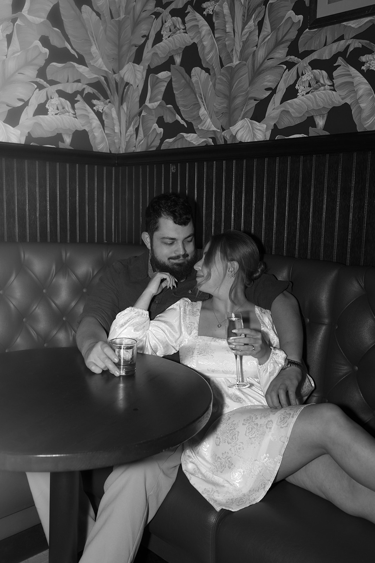 A elegant black and white photo of a couple sitting together at a booth drinking champagne for intimate Engagement Photo Session Ideas.