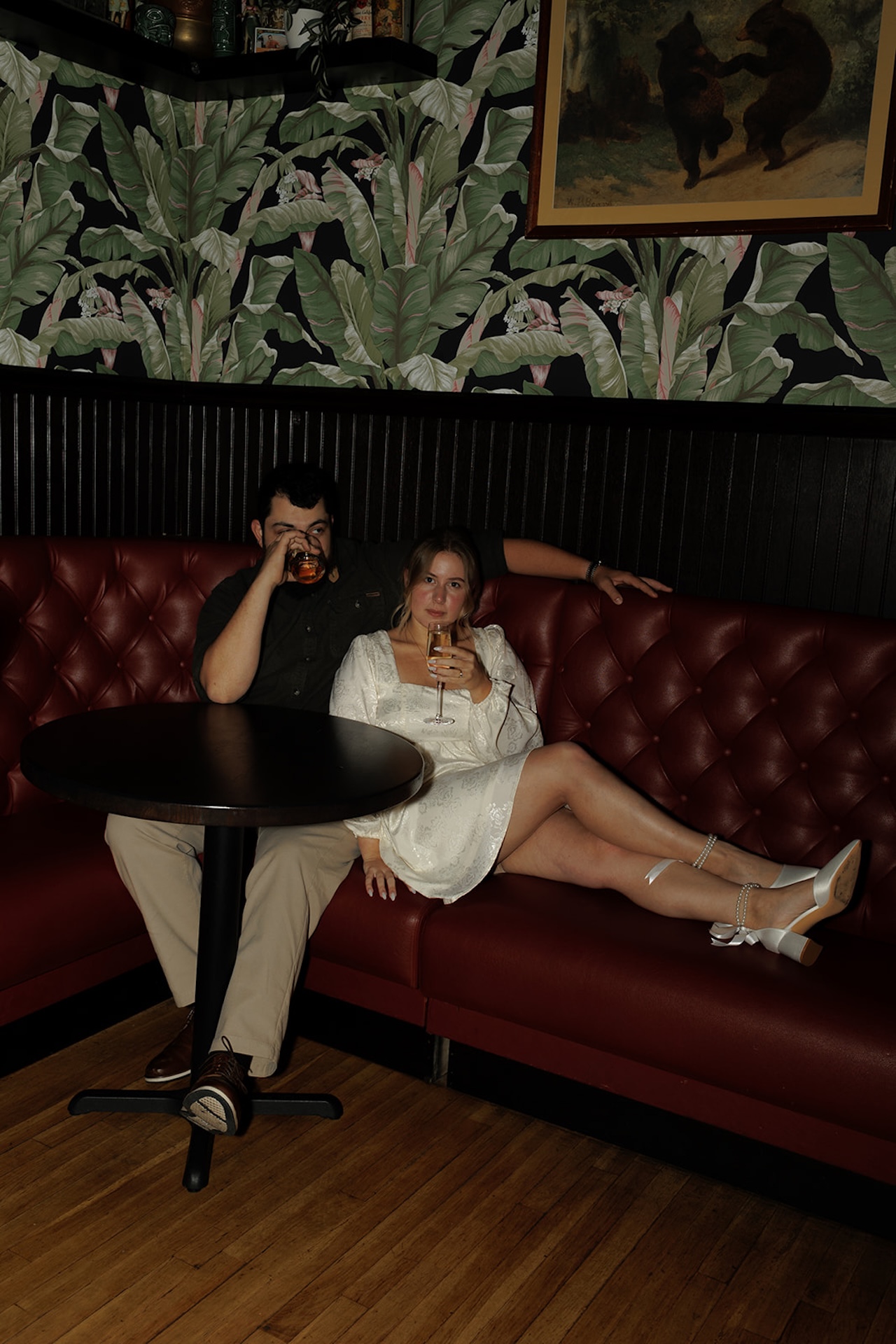 Couple sipping their drinks and sitting in a booth at speak easy during a flash photo