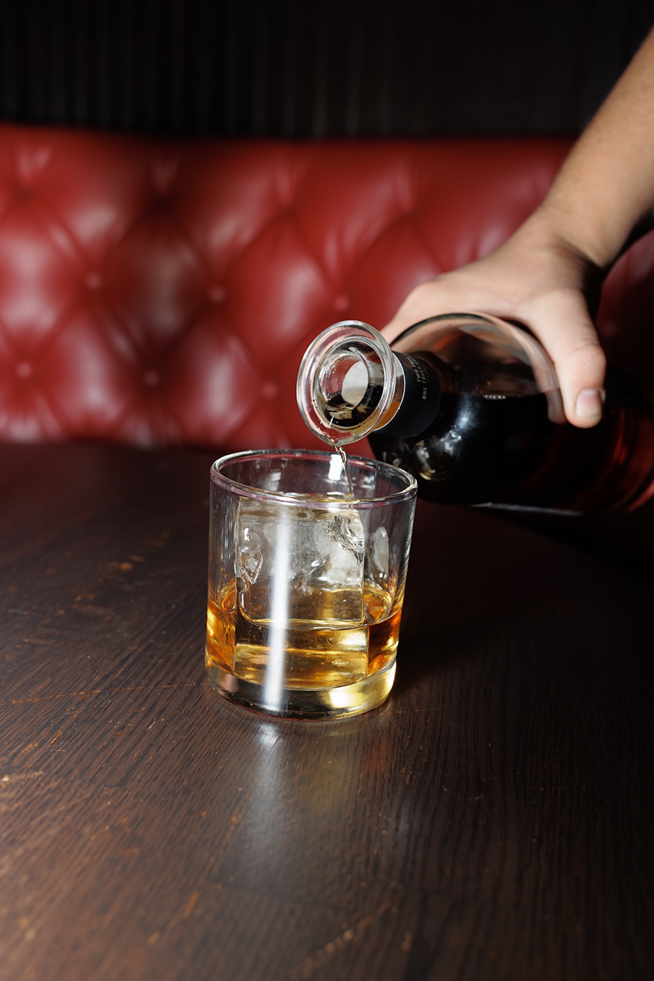 Close-up detail photo of a hand pouring a drink at a vintage bar, highlighting cozy atmosphere and candid moments during an engagement photo session.