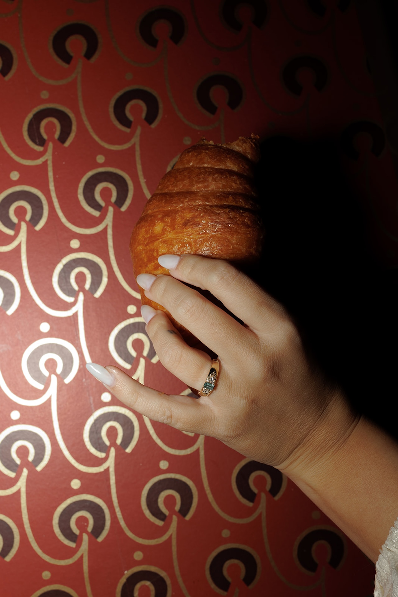 A flash photo of the bride to be holding a croissant in front of a wallpaper wall at a speakeasy.