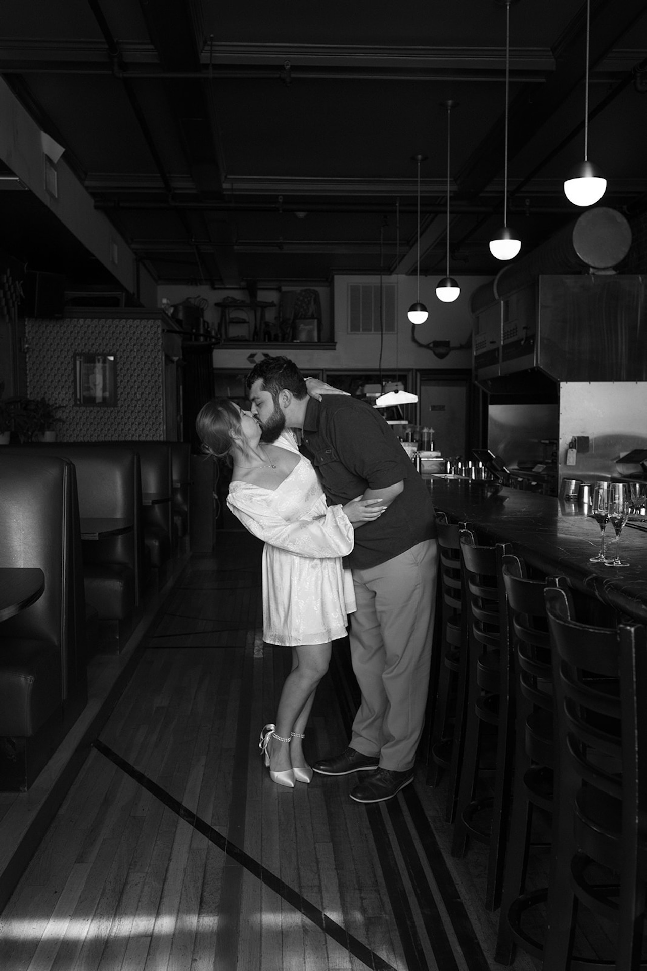 A black and white photo of a couple hugging and sharing a kiss in the middle of a speakeasy.