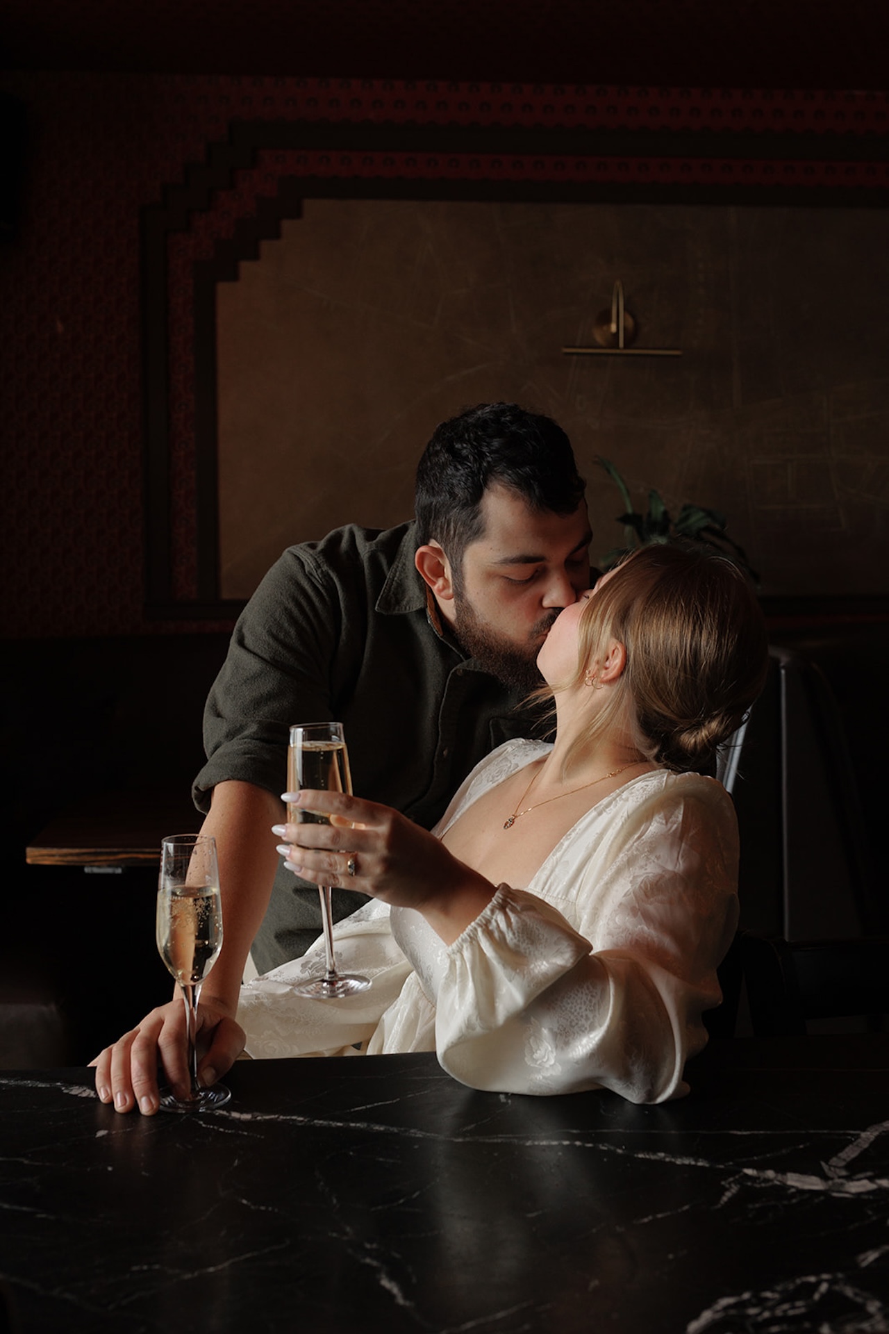Couple sharing a kiss at a bar while holding champagne glasses.