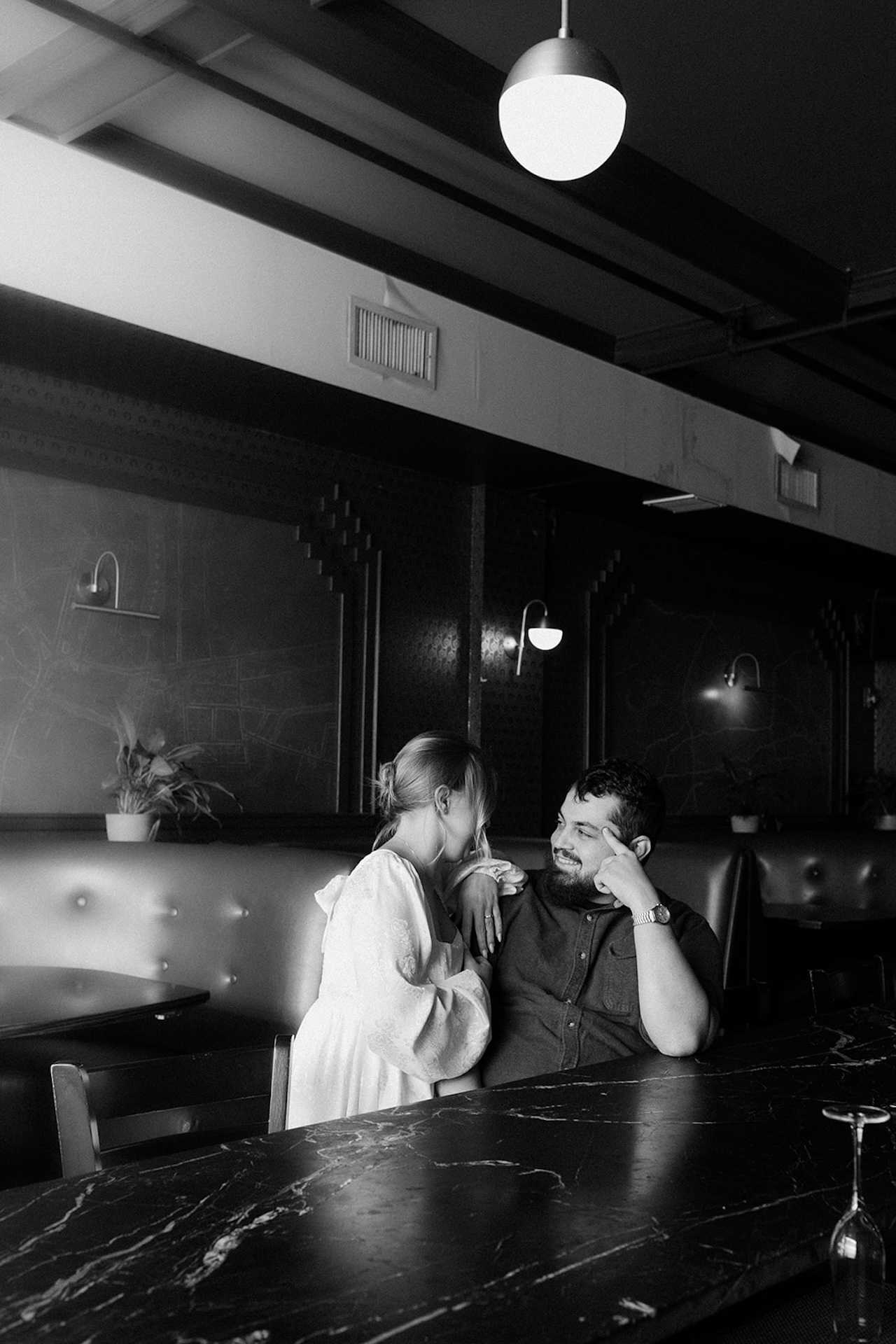 Engagement photo session ideas: A black and white photo of a couple sitting at a bar and laughing together during their engagement shoot.
