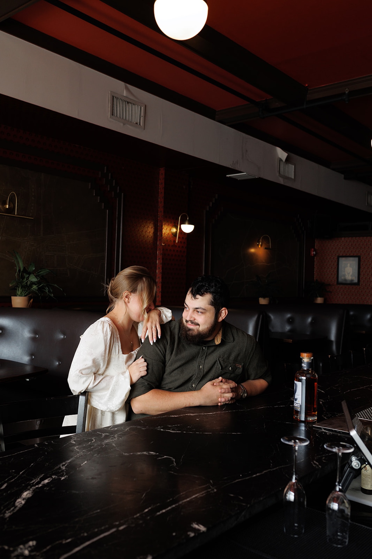 Engagement photo session ideas: A couple sitting at a bar and laughing together during their engagement shoot.