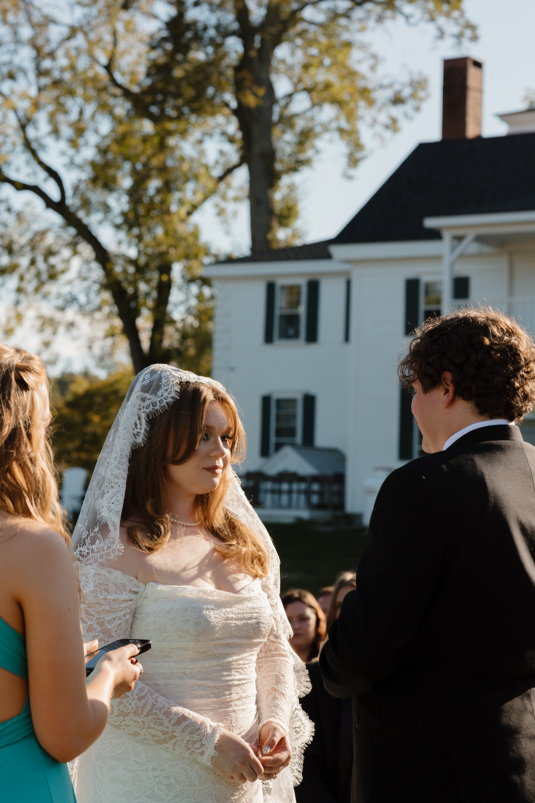 Bride listening to her now husband during vows at a Destination Wedding in Maine, sunlight illuminating her lace veil and long sleeve gown