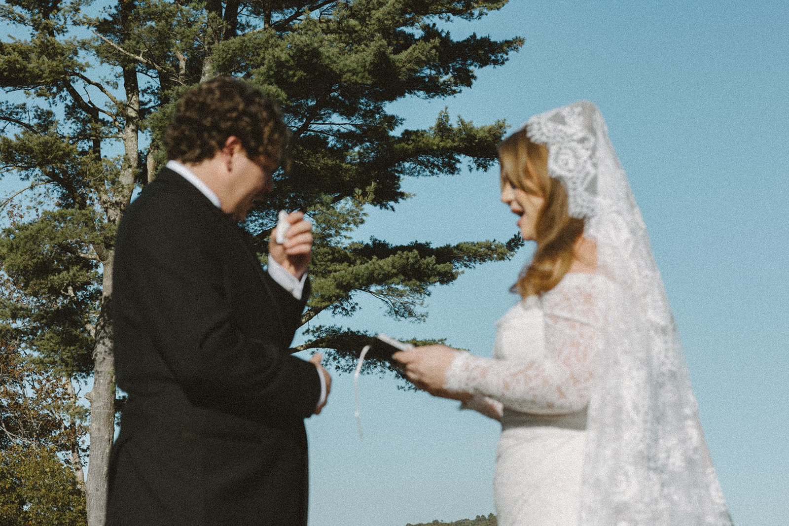 A film photo of the bride reading her vows to the groom as the groom uses a tissue to wipe his tears.