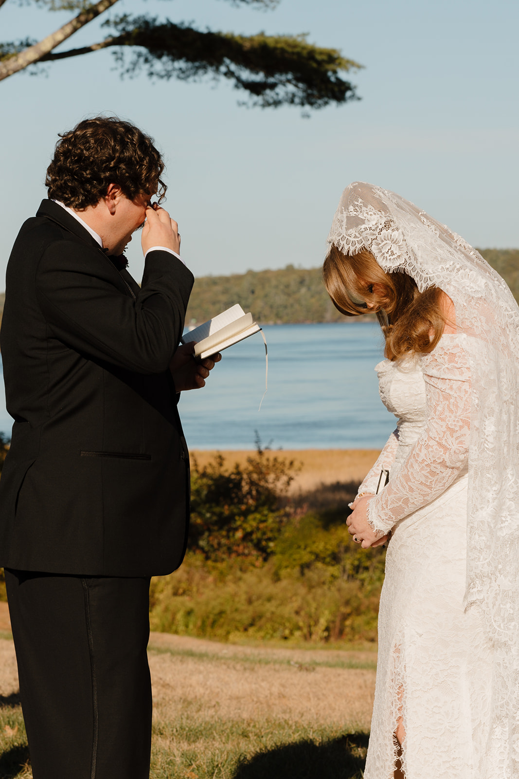Emotional vow exchange by the water during a Destination Wedding in Maine as the groom wipes away tears while reading from a small book