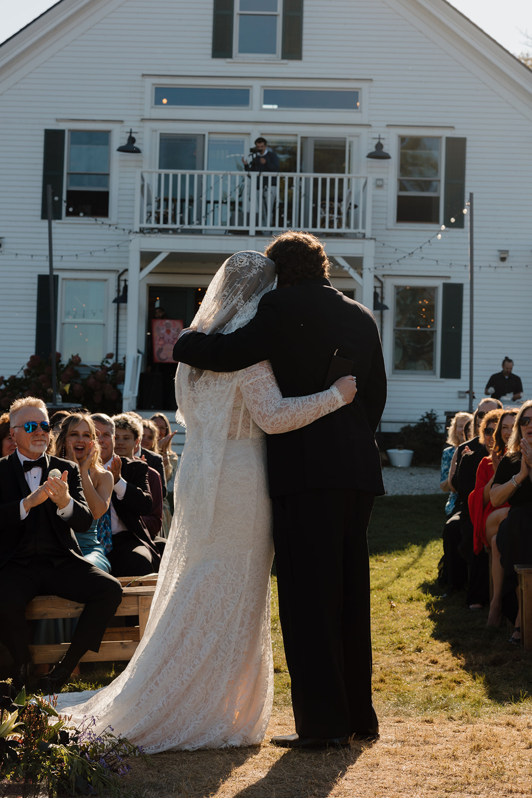 Bride and groom standing together after the ceremony during a Destination Wedding in Maine, framed by guests applauding and a white New England inn in the background