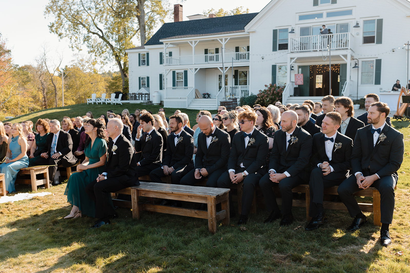 The wedding gueses and groomsmen sitting in the ceremony chairs with The 1774 Inn in the background during a Destination Wedding in Maine