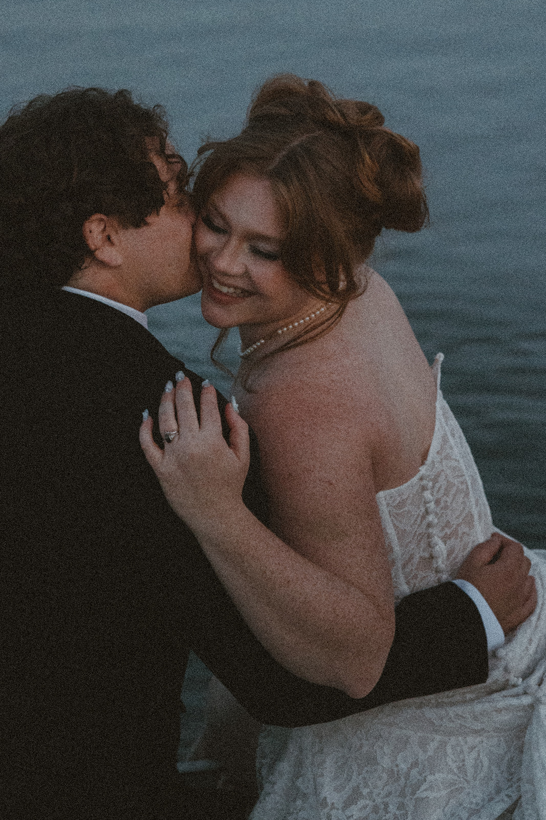 Moody dock portrait during a Destination Wedding in Maine as the bride and groom walk toward the water, framed by tall grasses and evening light