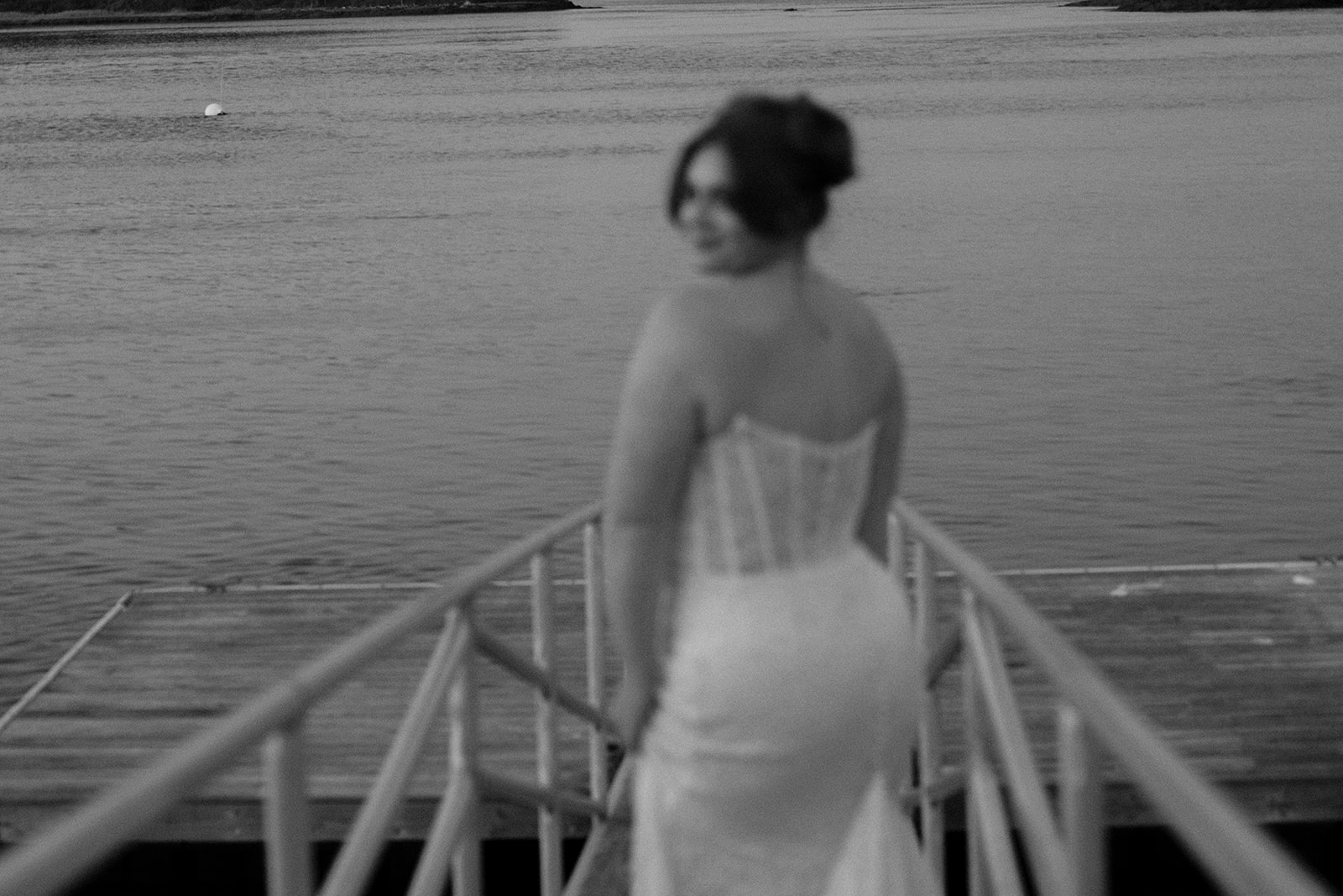 An elegant bridal portrait of the bride walking down to the dock of the water with her back towards the camera as she looks over her shoulder towards the camera.