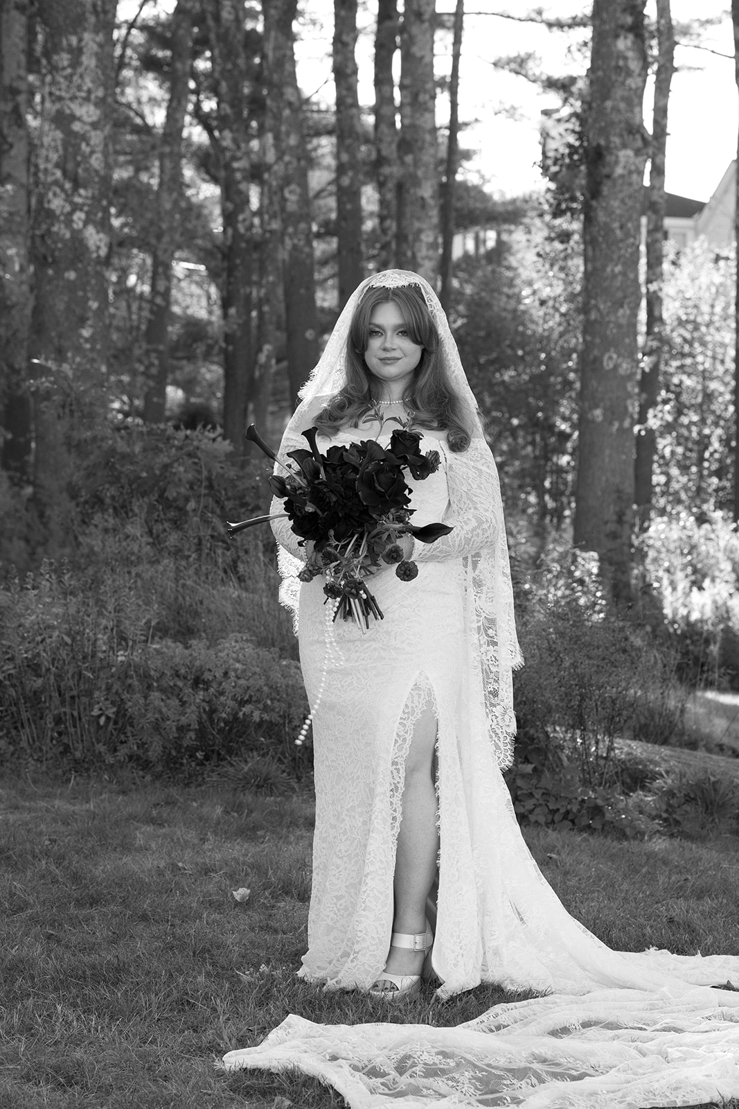 Black and white bridal portrait holding a dramatic bouquet during a Destination Wedding in Maine, lace gown and veil flowing in soft forest light