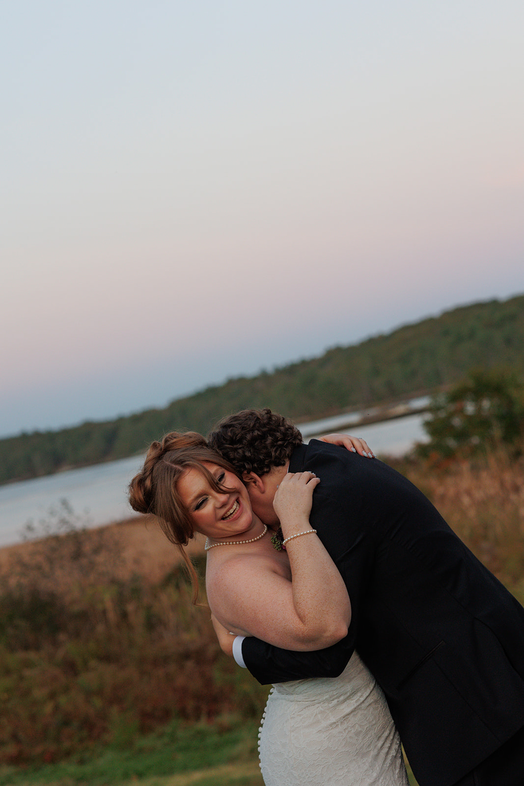 Candid sunset embrace during a Destination Wedding in Maine, the groom lifting the bride as she laughs against a coastal backdrop