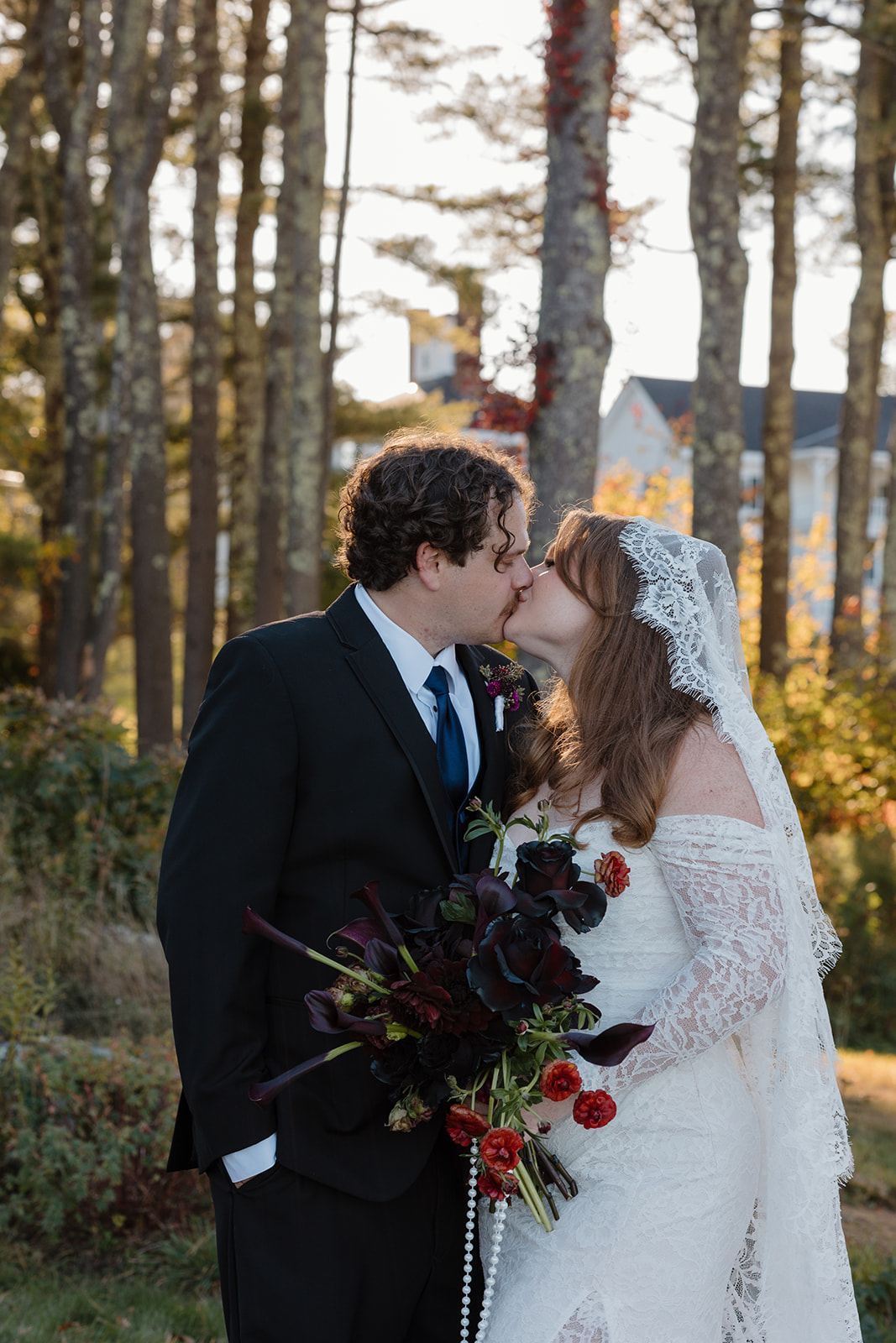 Bride and groom sharing a kiss at sunset, the bride holding a dark, moody bouquet with black calla lilies and deep red florals