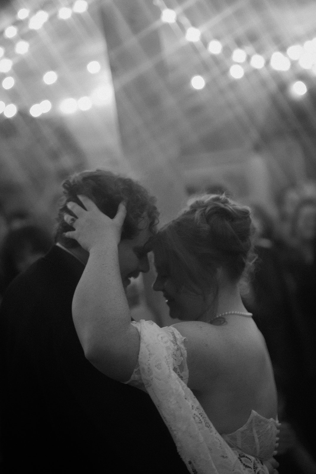 Emotional close-up of the couple touching foreheads during their first dance, captured in black and white with dreamy light streaks