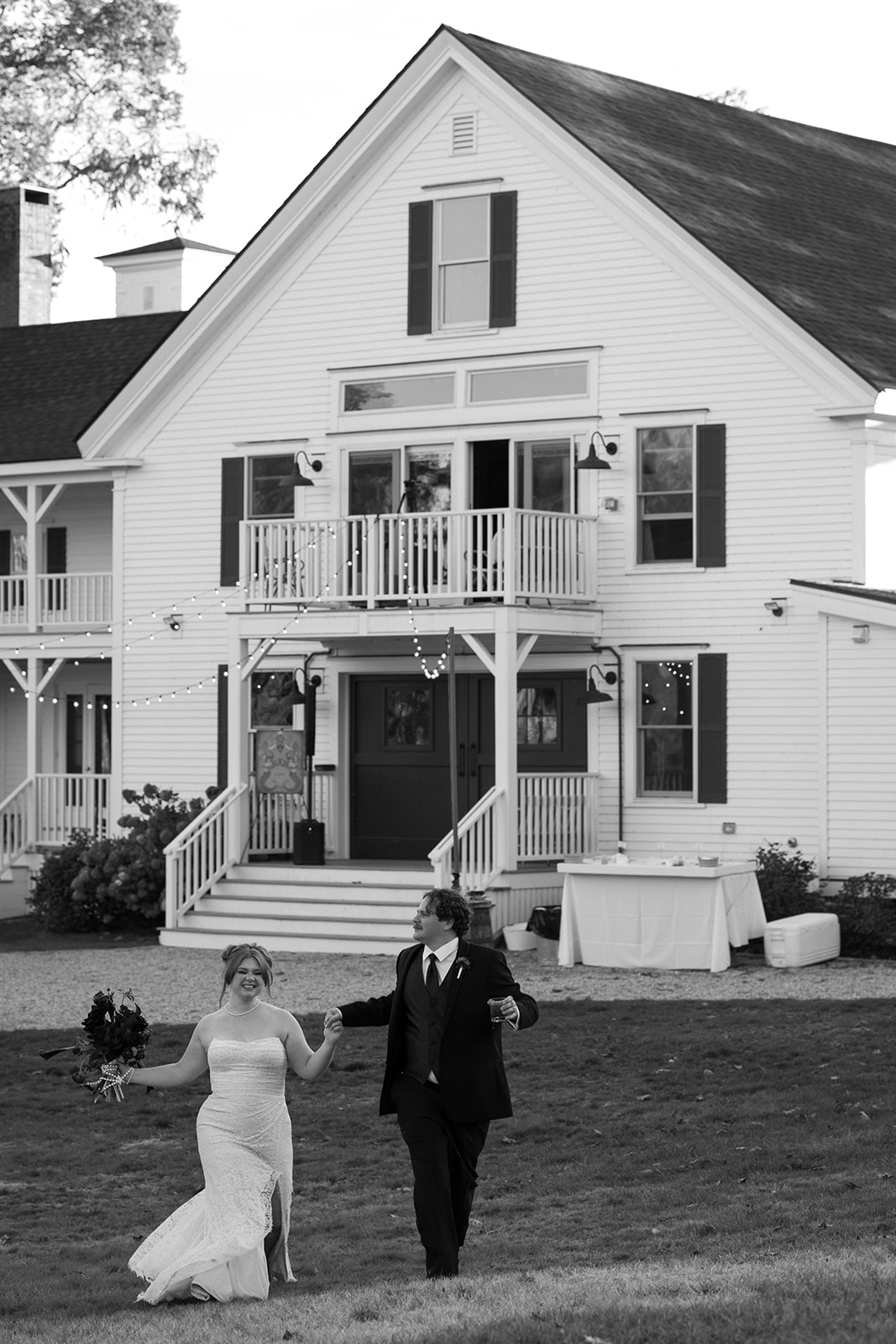 Wide black and white shot of the bride and groom celebrating together in front of a historic inn during a Destination Wedding in Maine, surrounded by classic New England architecture