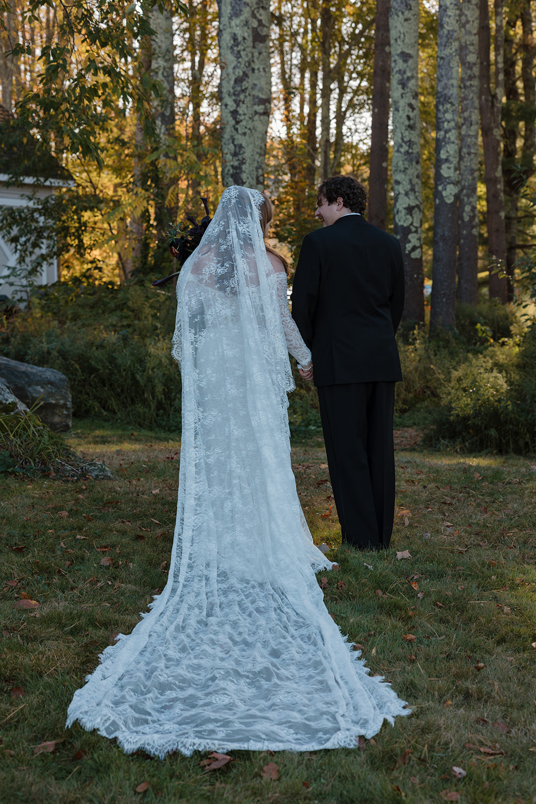 Bride and groom walking hand in hand at sunset, the bride holding a dark, moody bouquet with black calla lilies and deep red florals.