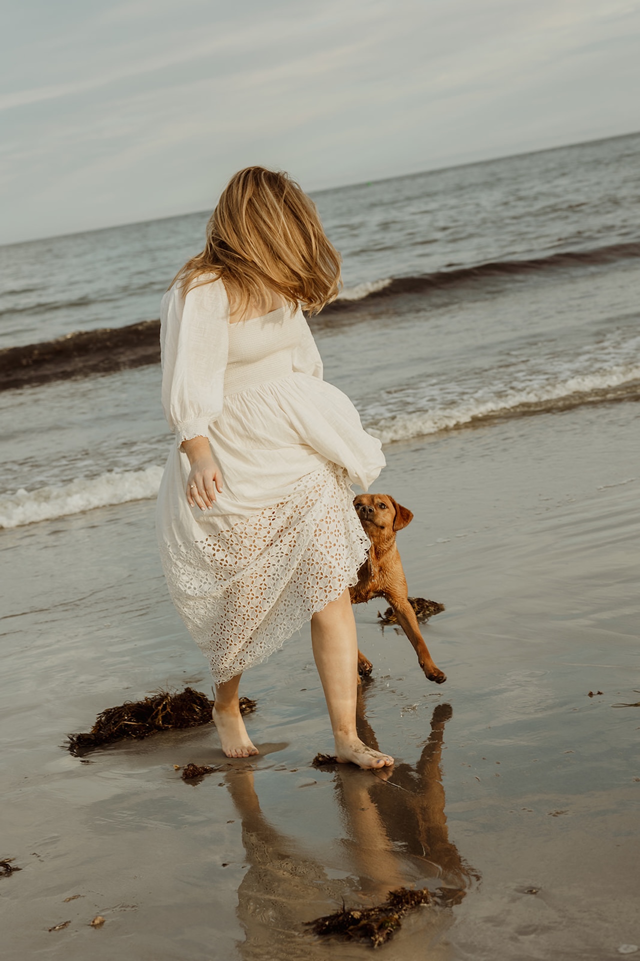 Candid engagement photo of bride-to-be walking along the beach with her dog near Nubble Lighthouse in York Maine.