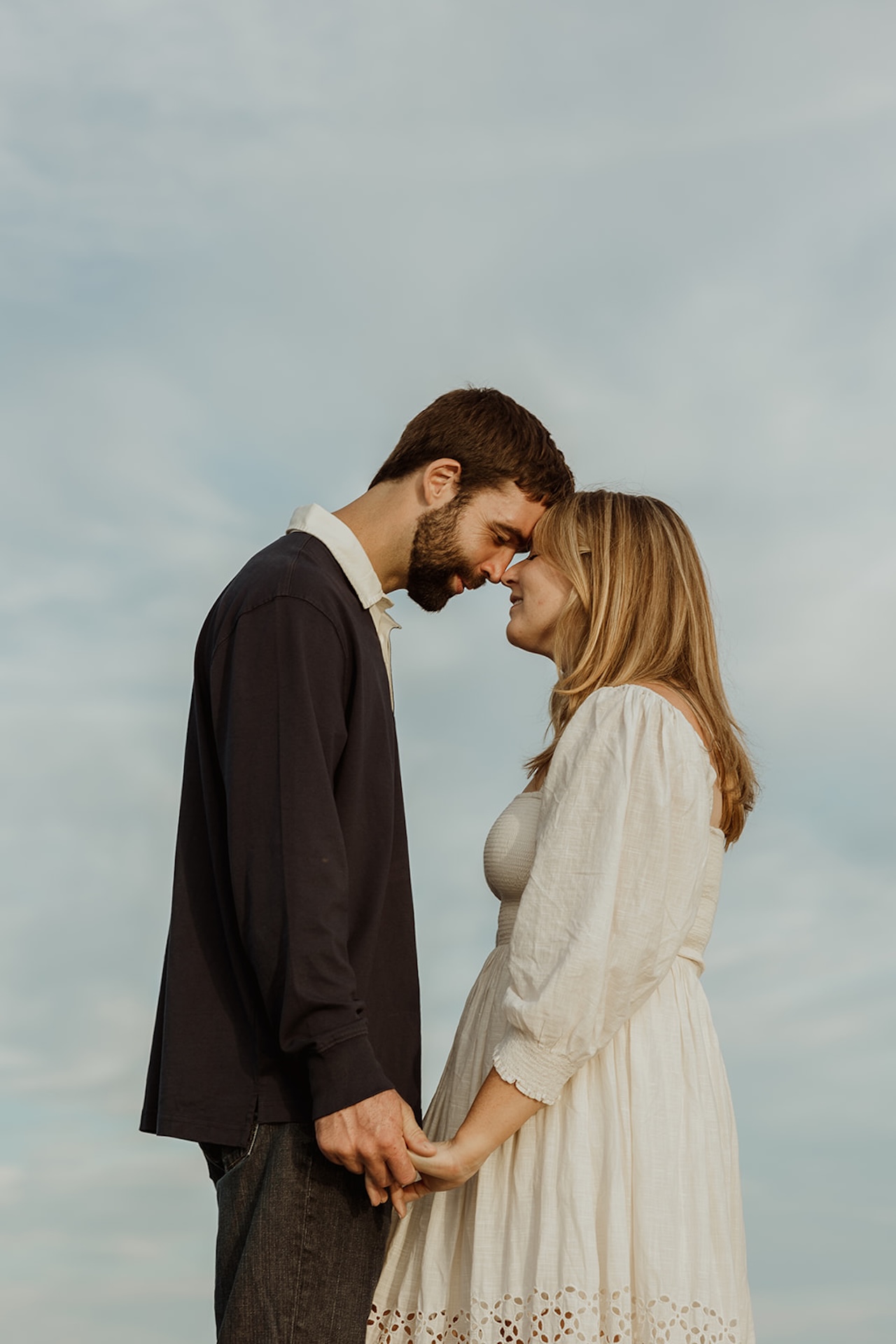 Romantic engagement photo of a couple touching foreheards on the sand near Nubble Lighthouse in York Maine with ocean waves behind them.
