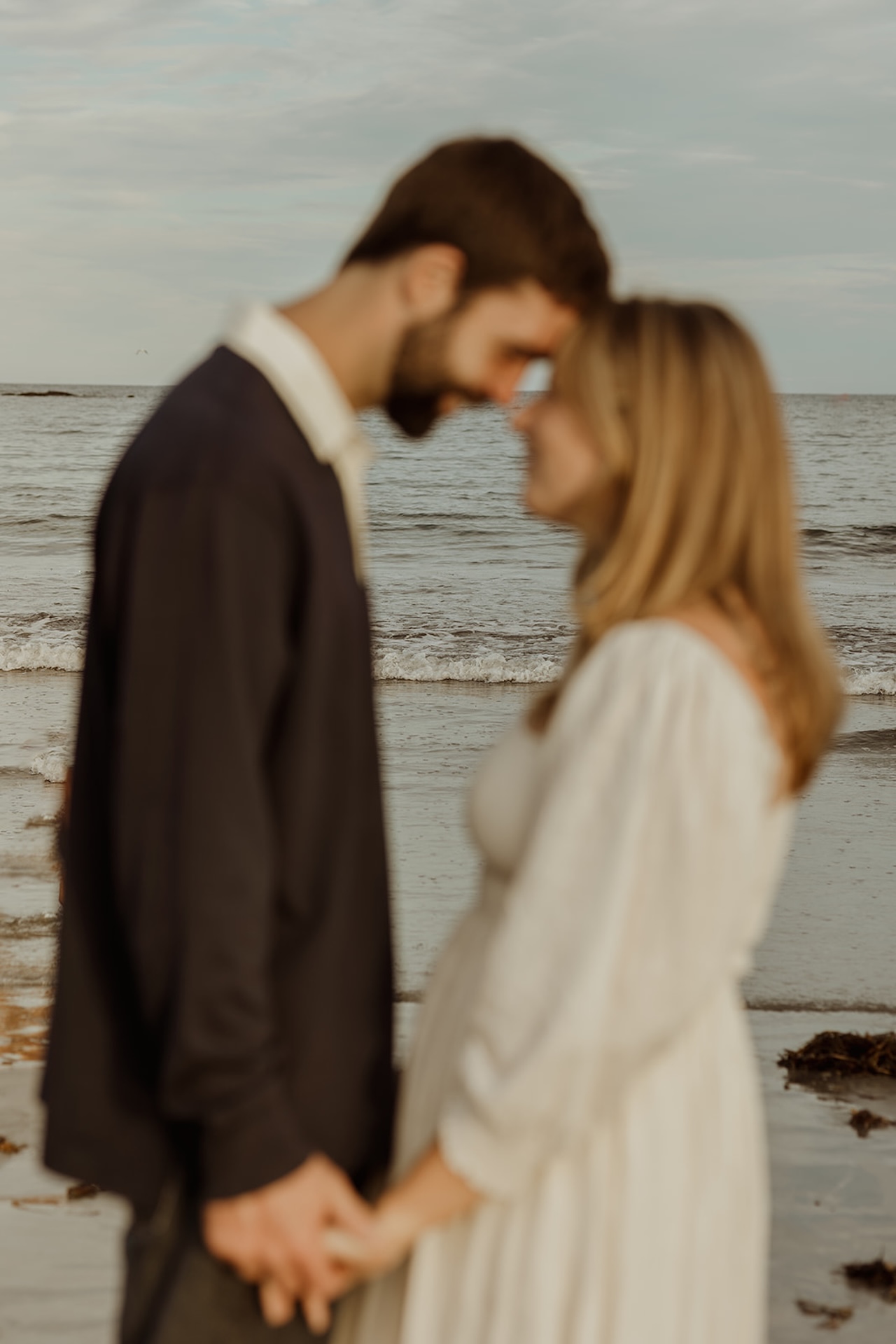 Blurred, dreamy engagement photo of couple leaning forehead to forehead by the ocean at sunset.