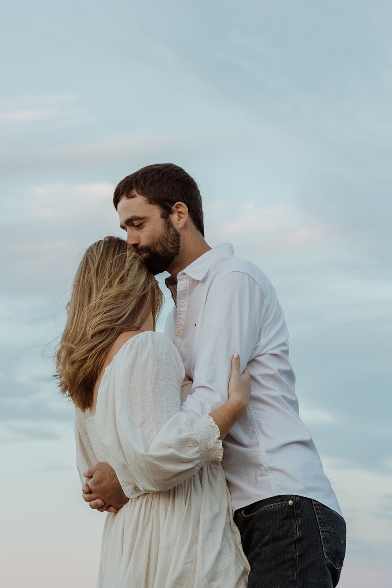 Romantic candid engagement portrait of couple laughing together while embracing on rocky beach coastline.