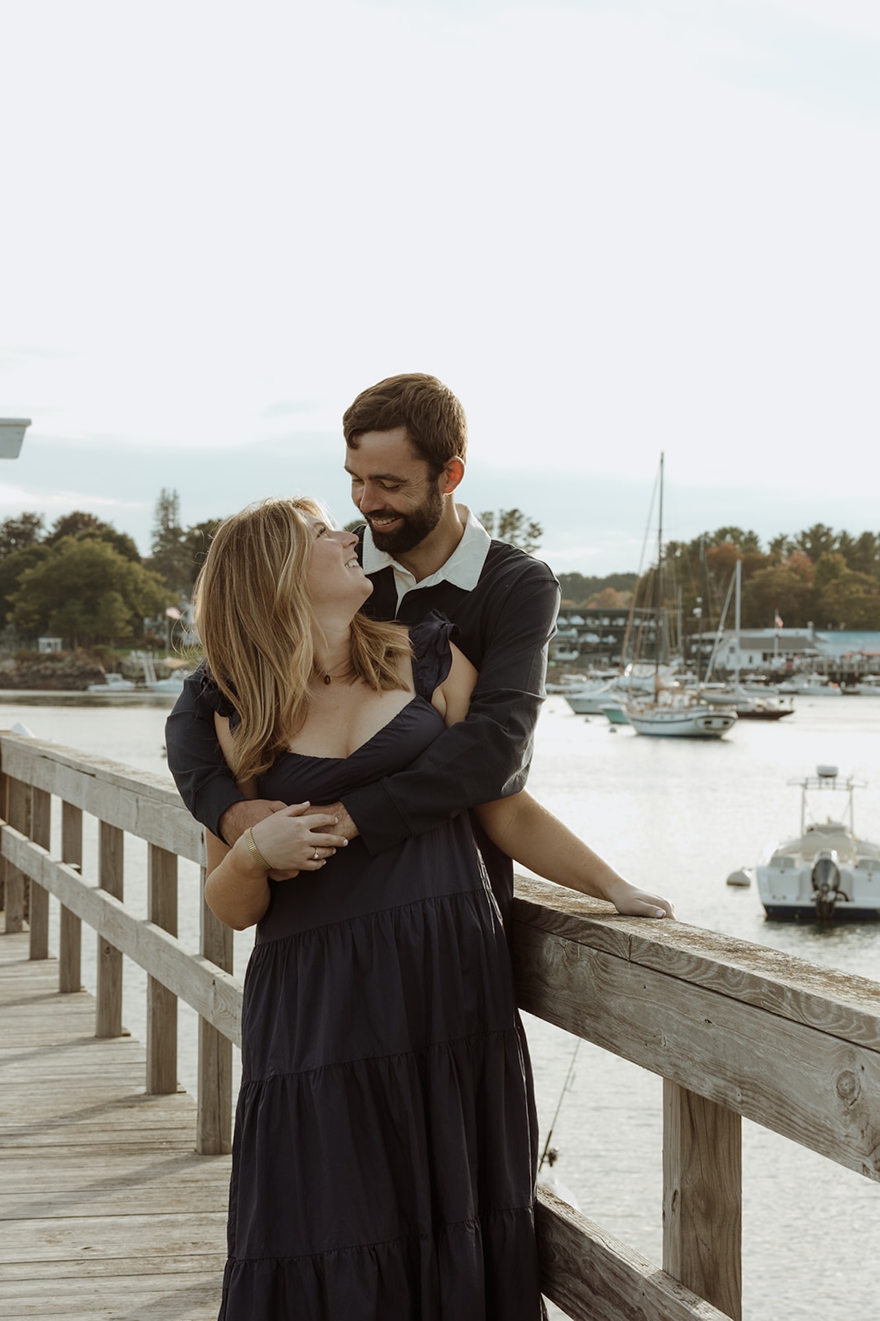 A couple standing on the dock at their wedding venue for their engagement photos with the boats in the background.